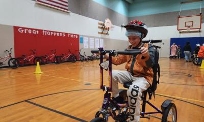 A student smiles while bicycling on an adaptive tricycle during gym class