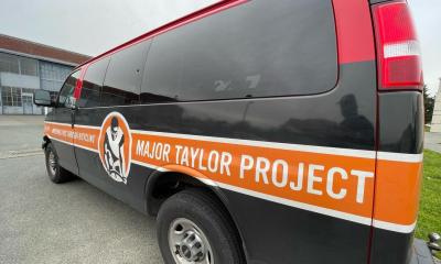 Black van with an orange strip down the middle with the words "Major Taylor Project" along the side