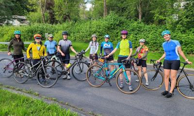 Group of nine riders from the women and non-binary program, leaning on their bikes smiling for the camera