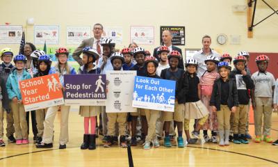 Students wear helmets and hold signs with messages like "stop for pedestrians" during a Let's Go class