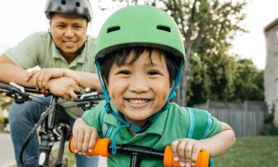Kid with helmet on a scooter with dad on bike.