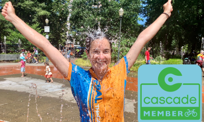 A woman raises her arms to celebrate a bike ride while getting doused with water. A Cascade member graphic is next to her