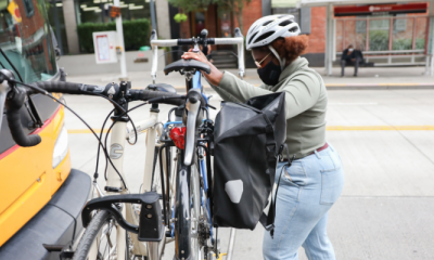 A woman places her bike on a rack on the front of a bus and secures it.
