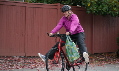A woman in a pink jacket bikes in the rain with a smile on her face